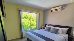 A hotel room with a large bed, a window with curtains, a ceiling light, and an air conditioning unit. - Beautiful home in gated community on private beach and Golf course in Costa Rica (Tambor)
