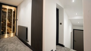 A modern hallway with a radiator, a vertical panel, and a door leading to another room. - Rose House (Boston)