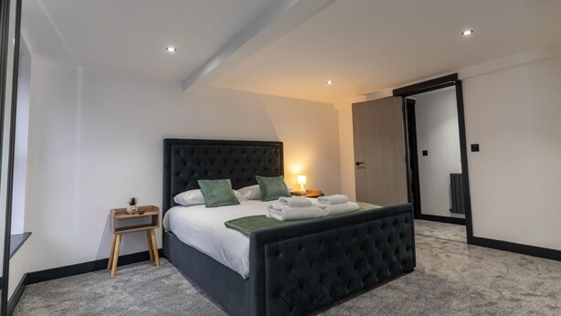 A modern bedroom with a large bed, a bedside table, and a mirror. - Rose House (Boston)