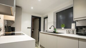 A modern kitchen with white cabinetry, a black countertop, and a window with blinds. - Rose House (Boston)