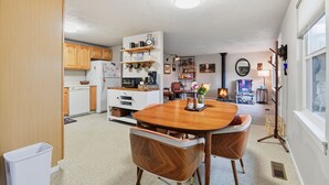 A compact kitchen with wooden cabinets, a white refrigerator, and a dining table with two chairs. - Hoops & Hygge Private Sport Court Retreat 3 Bedroom Home (Lakewood)
