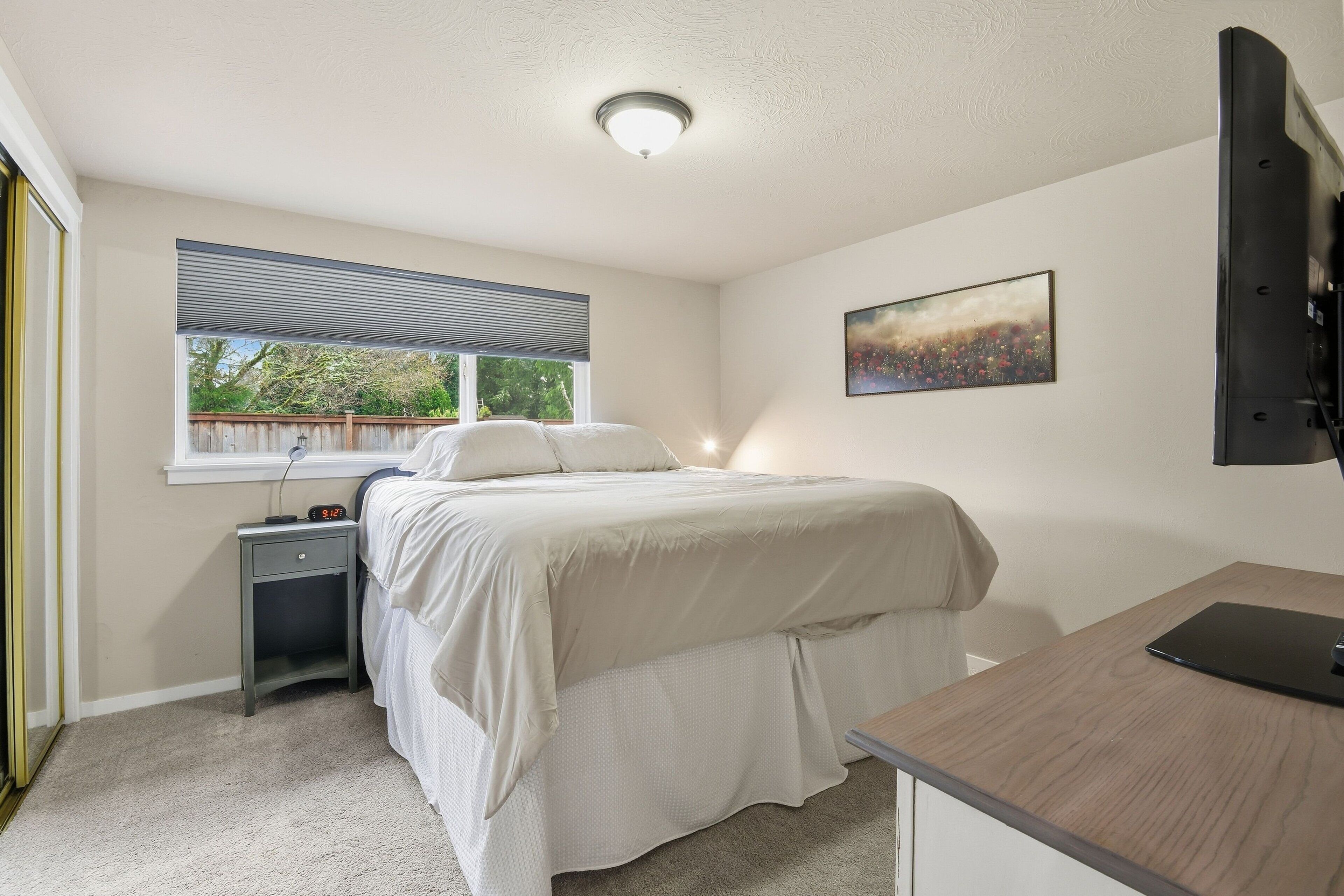 Quarto com cama, mesa de cabeceira, escrivaninha e janela com persianas.