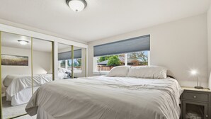 A bedroom with a large bed, a wardrobe, a bedside table, and a window with blinds. - Hoops & Hygge Private Sport Court Retreat 3 Bedroom Home (Lakewood)