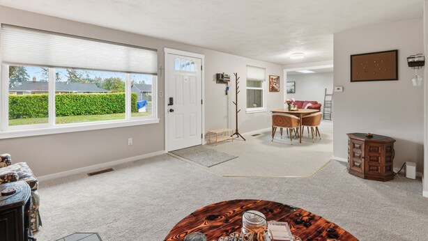 A spacious living room with large windows, a dining area, and a small kitchen. - Hoops & Hygge Private Sport Court Retreat 3 Bedroom Home (Lakewood)