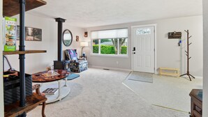 A spacious living room with a large window, a fireplace, a coat rack, and a door leading outside. - Hoops & Hygge Private Sport Court Retreat 3 Bedroom Home (Lakewood)