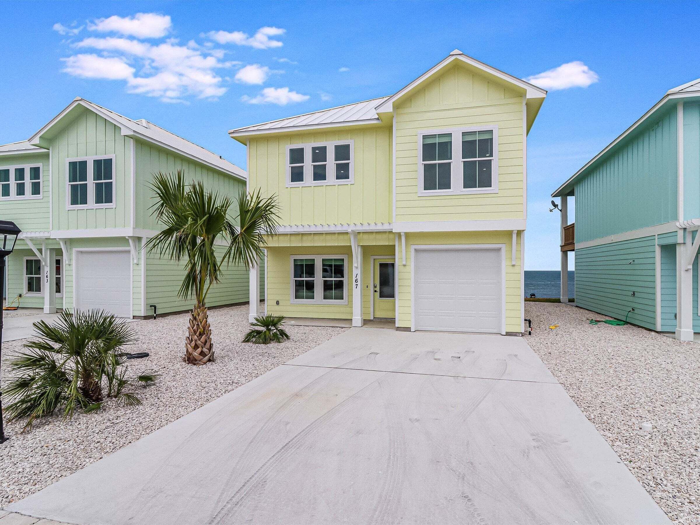 A two-story building with a garage, a driveway, and a small palm tree in front.