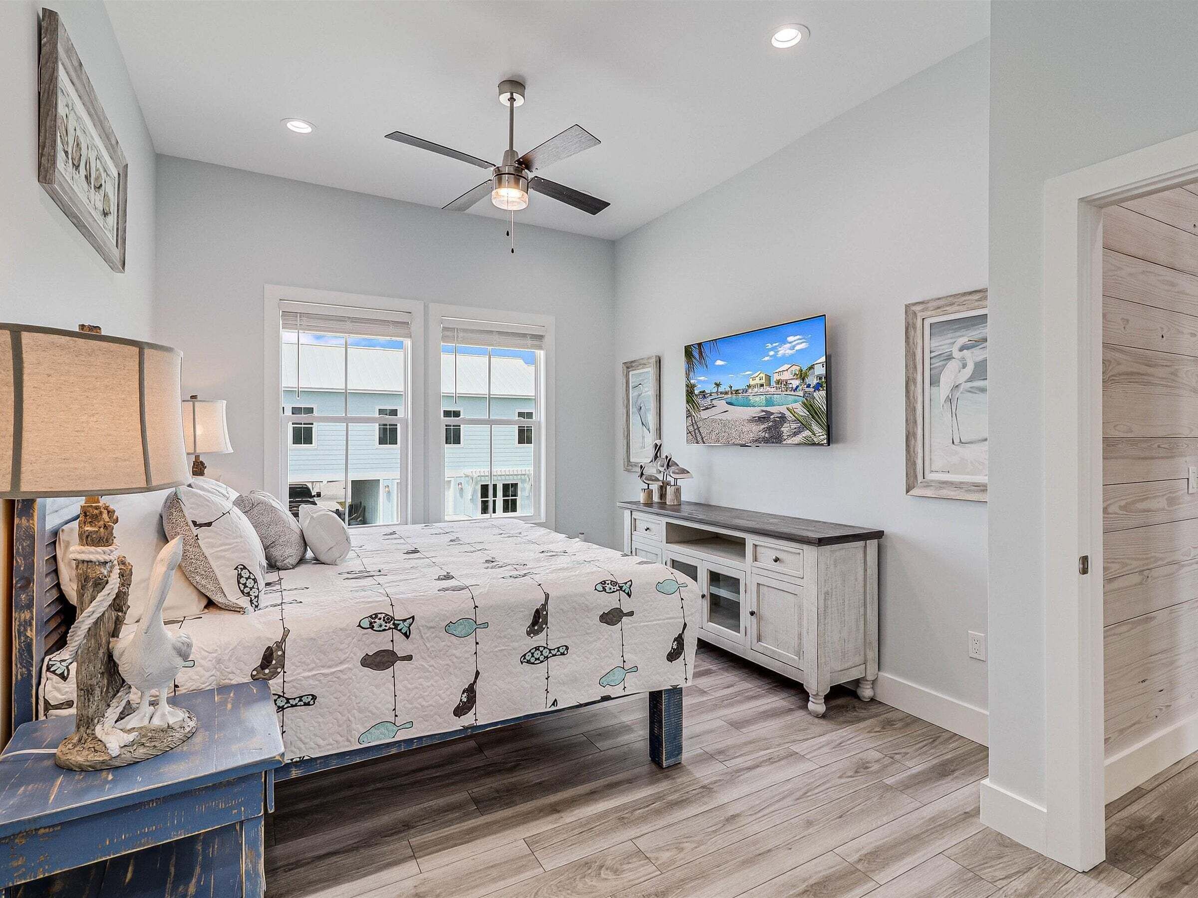 A bedroom with a bed, a desk, a ceiling fan, and a TV on the wall.