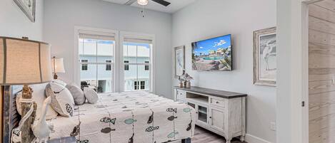 A bedroom with a bed, a desk, a ceiling fan, and a TV on the wall.