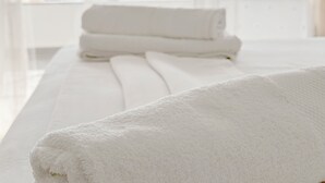 Ein Hotelzimmer mit großem Fenster, einem Bett mit weißer Bettwäsche und einem ordentlich gefalteten Handtuch auf dem Bett.