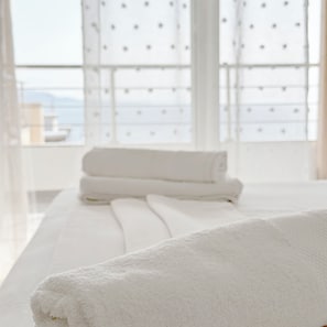 Une chambre d’hôtel avec une grande fenêtre, un lit recouvert de draps blancs et une serviette soigneusement pliée posée sur le lit.