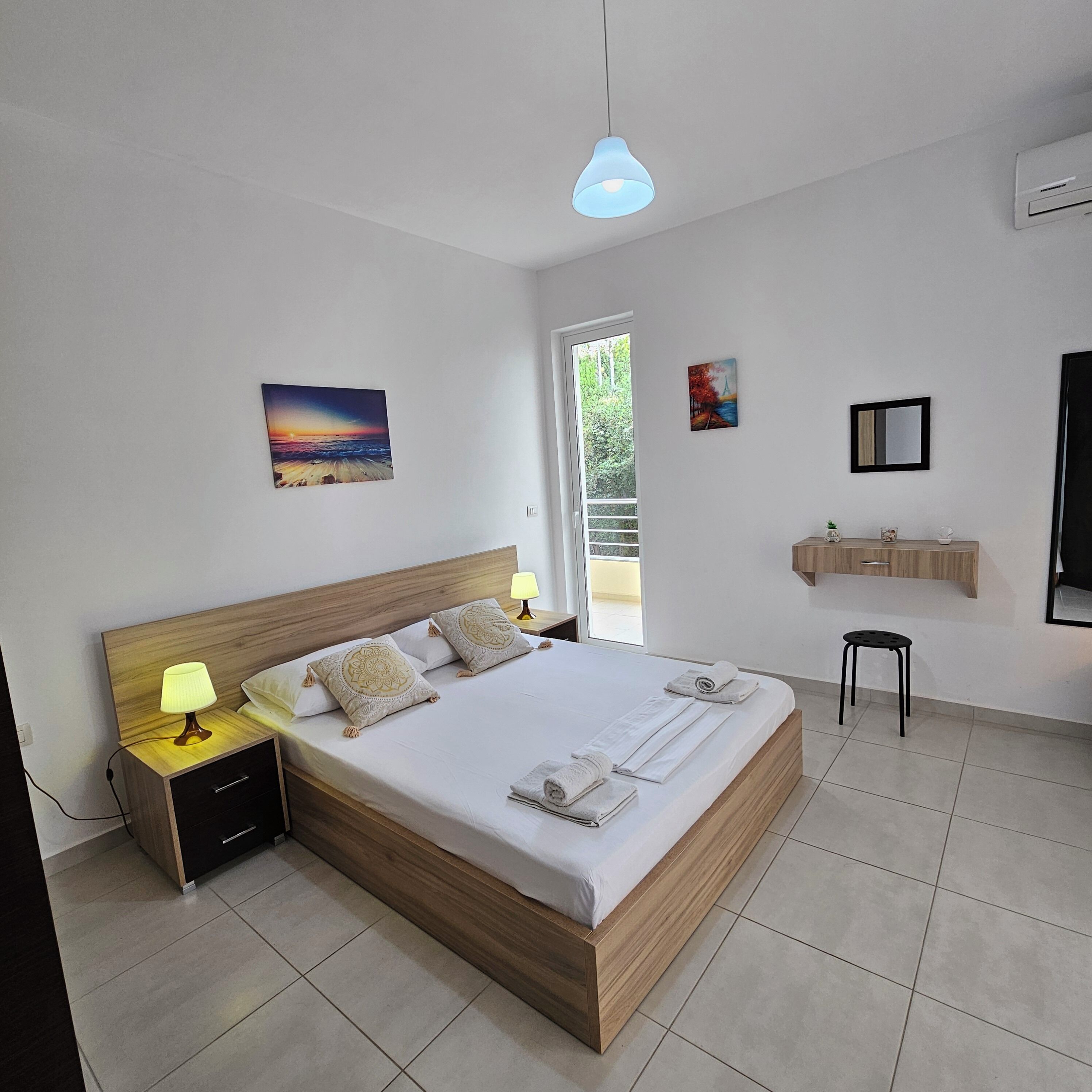 Una camera da letto moderna con un letto di legno, lampade sui comodini, vista sull'esterno e un piccolo bagno.