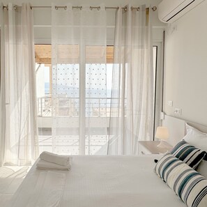 A hotel room with a bed, a nightstand with a lamp, and a view of a balcony with a railing. - Ares Summer Apartments (Sarandë)
