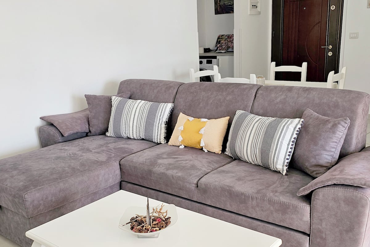 A grey sectional sofa with multiple cushions, a white coffee table, and a small decorative plant.