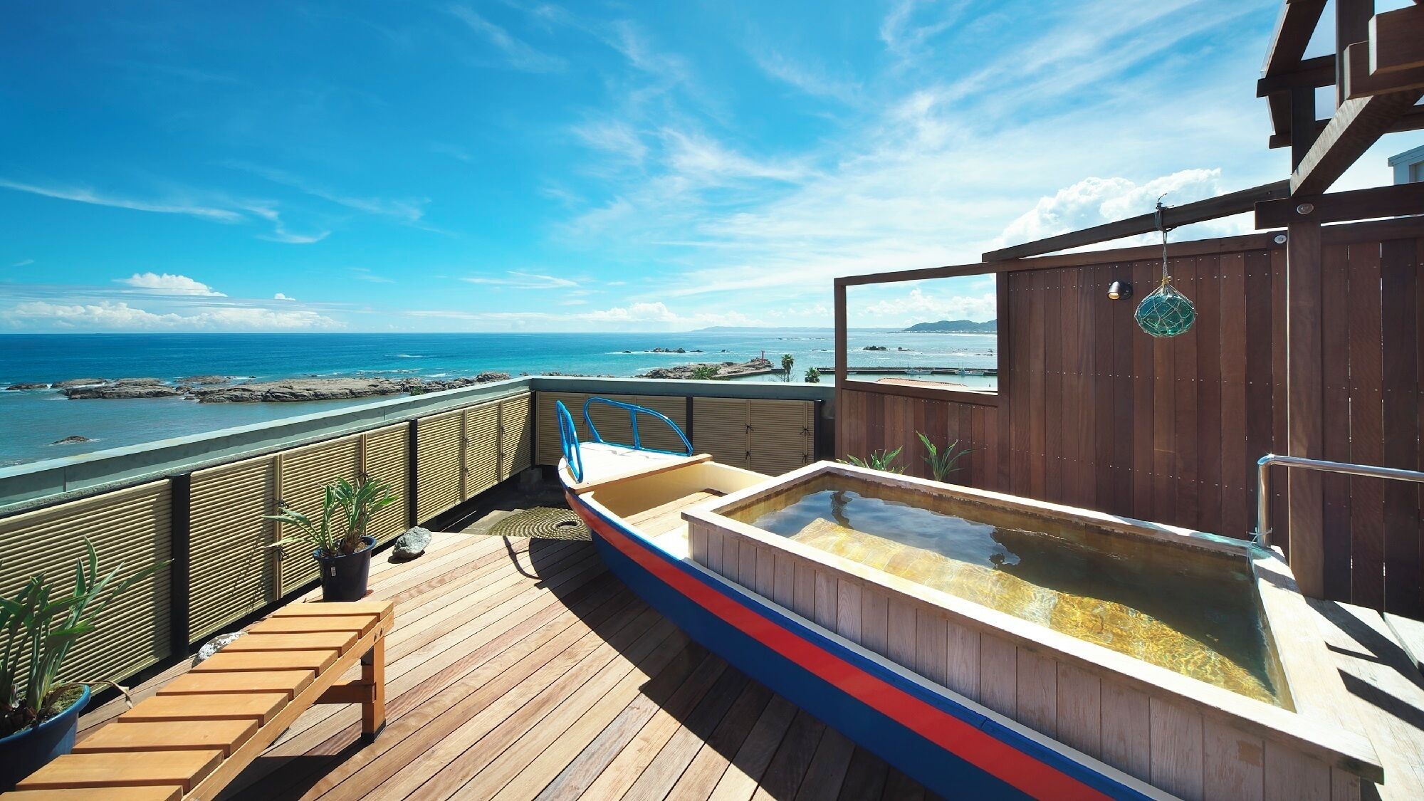 Een houten terras met een jacuzzi, potplanten en uitzicht op de oceaan.