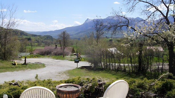 A patio with two white chairs, a small fire pit, and a view of a rural landscape with mountains and a house in the distance.