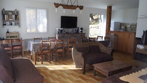 A living room with a sofa, chairs, a dining table, a television, and a kitchen area.