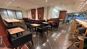 A modern restaurant with wooden tables and black chairs, a tiled floor, and a glass partition wall. - Utility Hotel Cooju (Kawagoe)