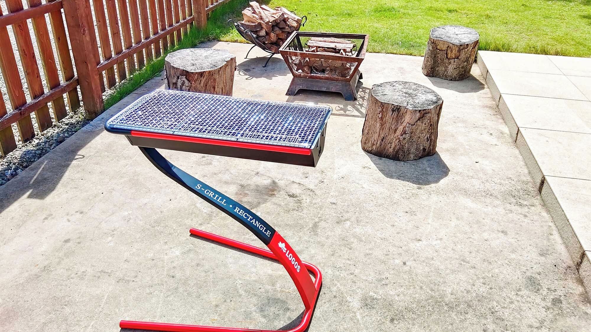 Un patio con una parrilla de metal, leña y una mesa de metal.