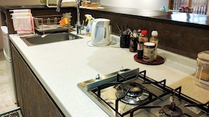 Una cocina con estufa a gas, un fregadero y diversos utensilios como una tetera, botellas y cubiertos.
