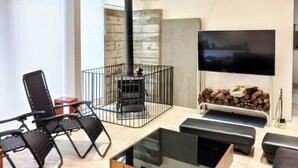 Una sala de estar moderna con chimenea, un televisor montado en la pared y una zona de estar con sillas y un banco.