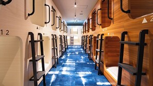A hotel corridor with bunk beds, numbered room signs, and a blue patterned carpet.