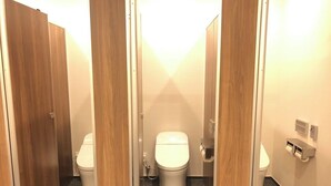 A public restroom with wooden partitions, white toilets, and a paper towel dispenser.