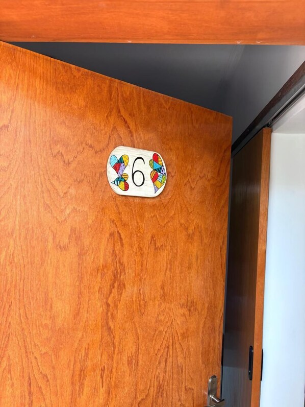 Une porte en bois ornée d’une plaque portant le numéro 6 et d’un motif coloré.
