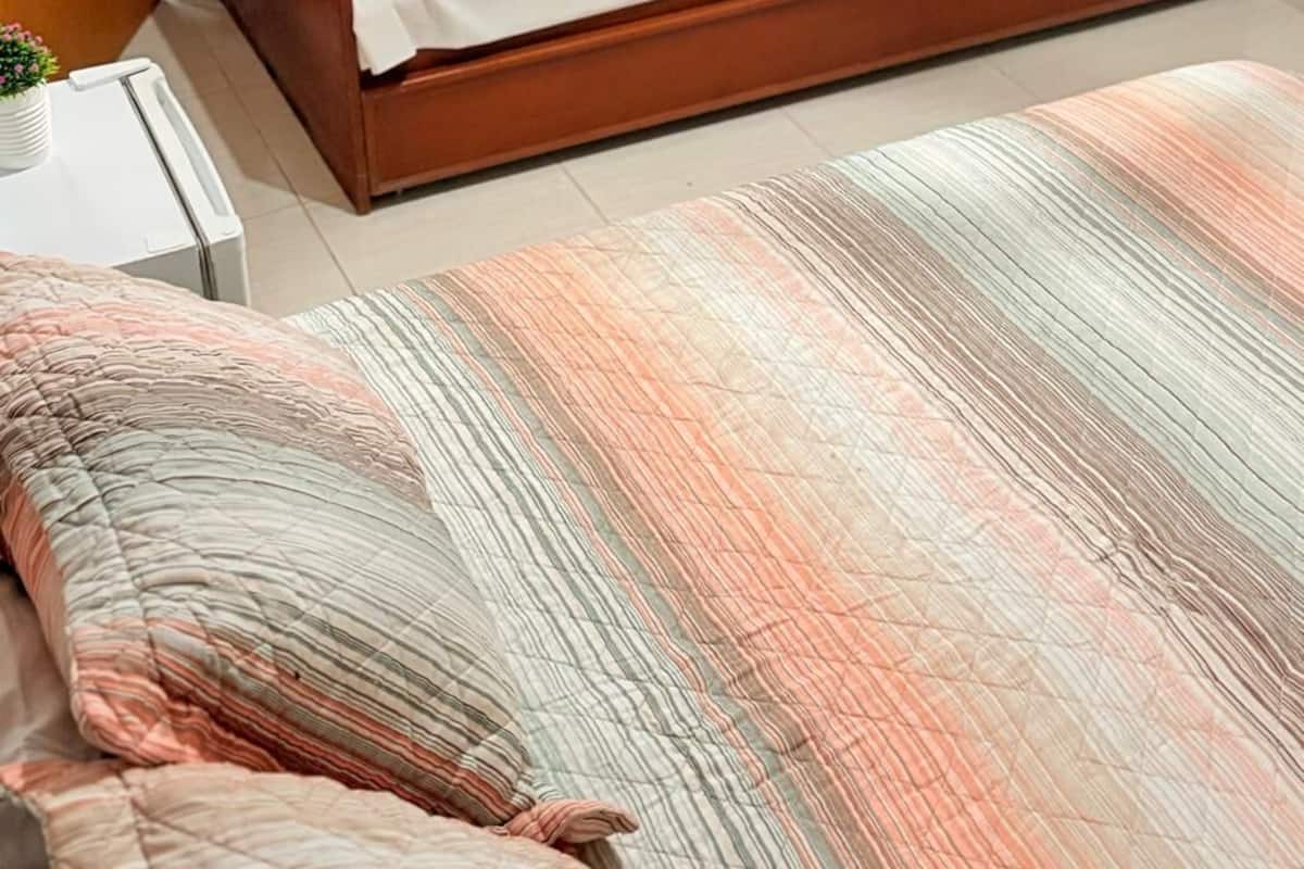Een eenpersoonsbed met houten frame, een witte matras en opgerolde handdoeken erop.
