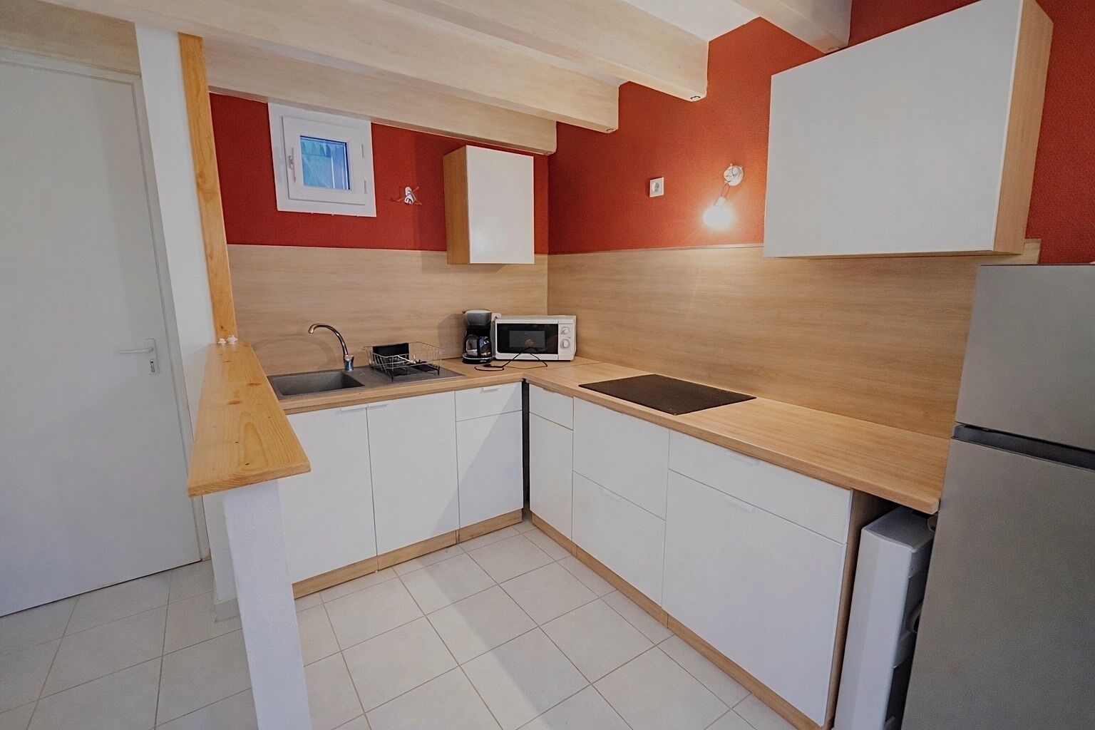 Een kleine keuken met witte kastjes, een houten aanrecht, een magnetron en een koelkast.
