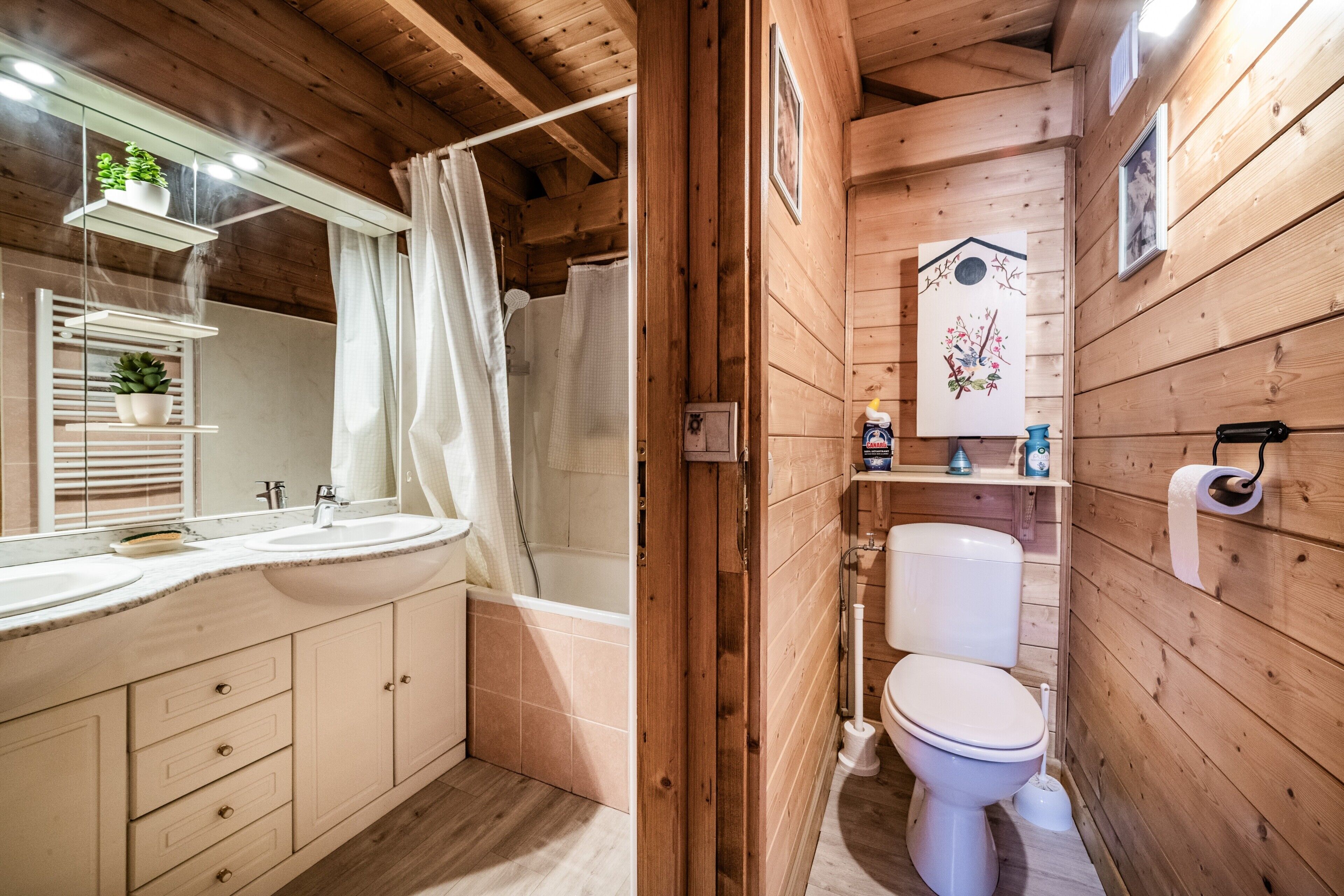 A wooden cabin bathroom with a bathtub, toilet, and a mirror with a shelf holding plants.