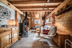 Ein Holzblockhaus mit Essbereich, einer Couch, einem Sessel, einem Kamin und einer Uhr an der Wand.