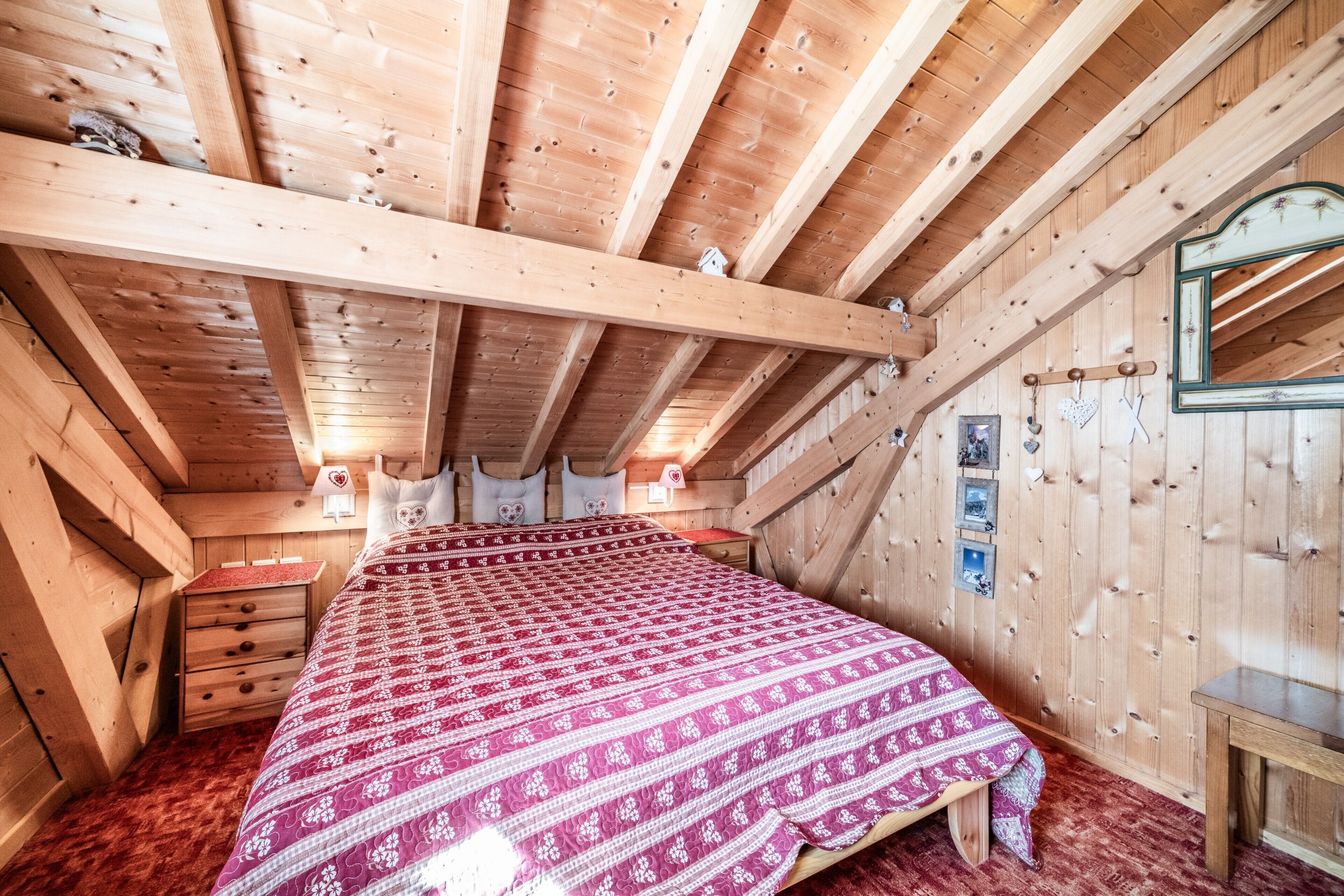 A wooden cabin bedroom with a bed, bedside tables, a mirror, and a wooden ceiling.