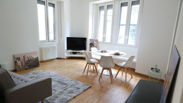 Uma sala de estar moderna com sofá, mesa de jantar, cadeiras, televisão de tela plana e janelas amplas.