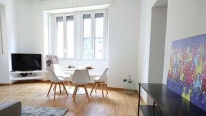 Uma sala de estar moderna com televisão, mesa de jantar, cadeiras, tapete e obras de arte.