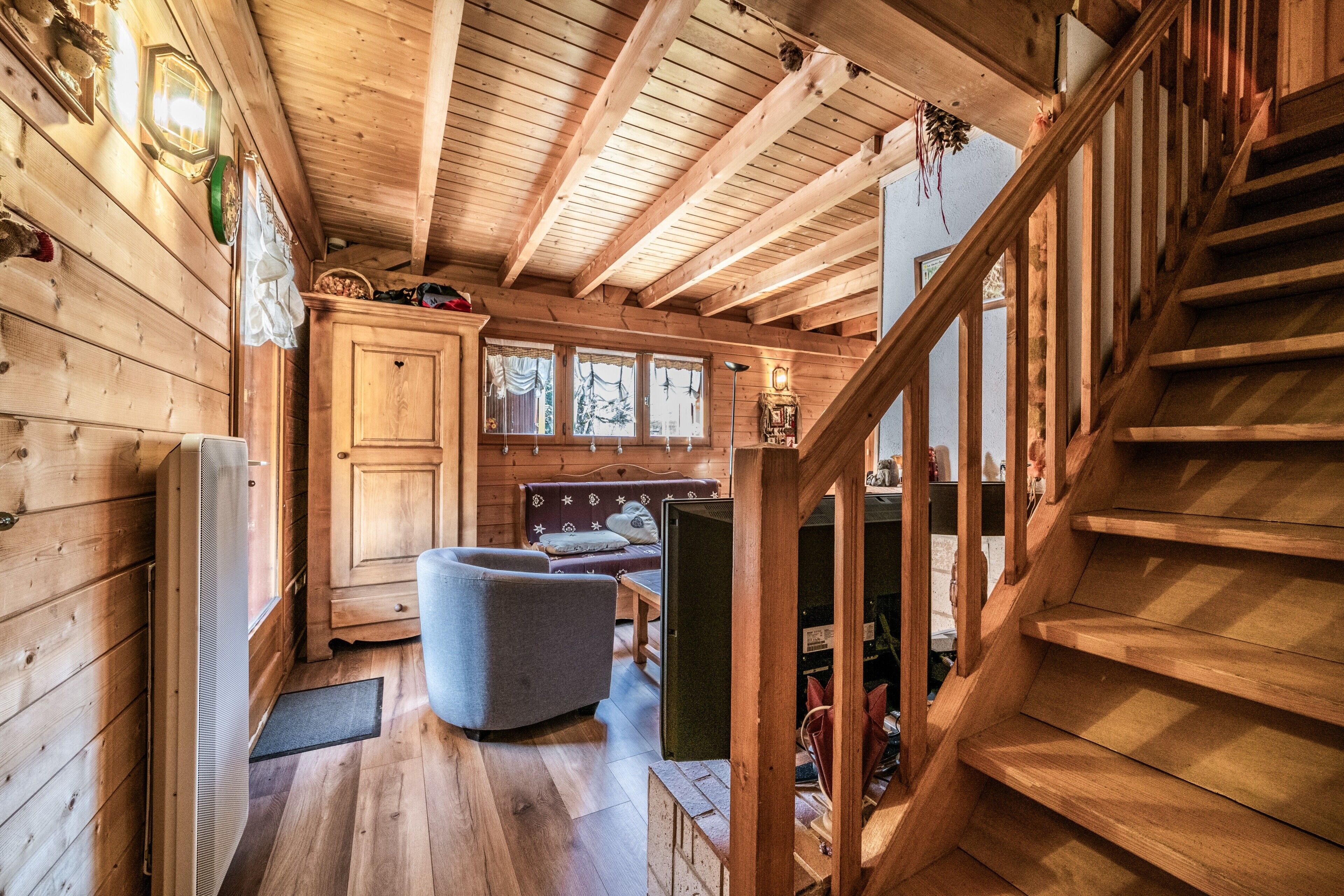 A wooden cabin interior with a staircase, a sofa, and a cabinet.