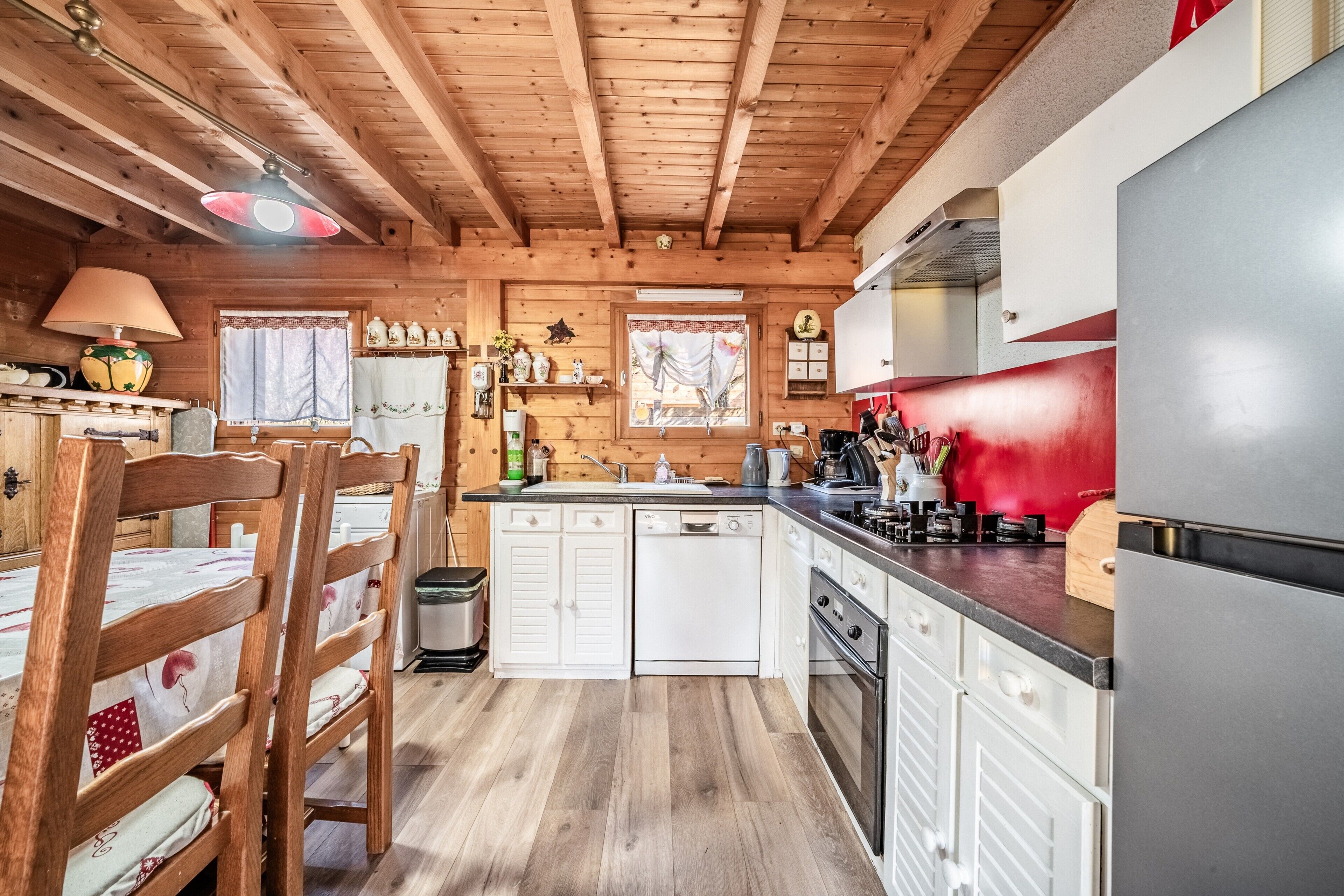 Interior de una cabaña de madera con cocina, comedor y un reloj en la pared.