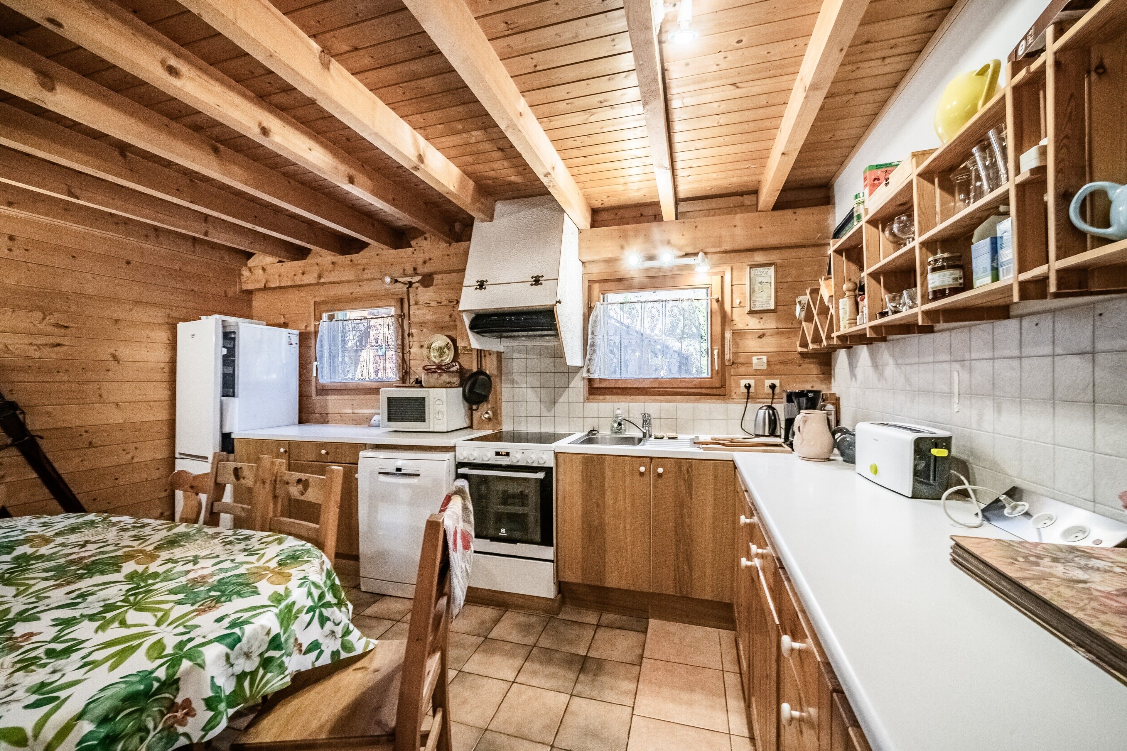 Interior de una cabaña de madera con cocina, comedor y una cama con colcha estampada.
