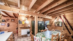 A wooden cabin interior with a dining area, kitchen, and a ski rack. - Chalet “8p Simple - Les Mésanges” with Mountain View, Private Terrace, and Wi-Fi (Verchaix)