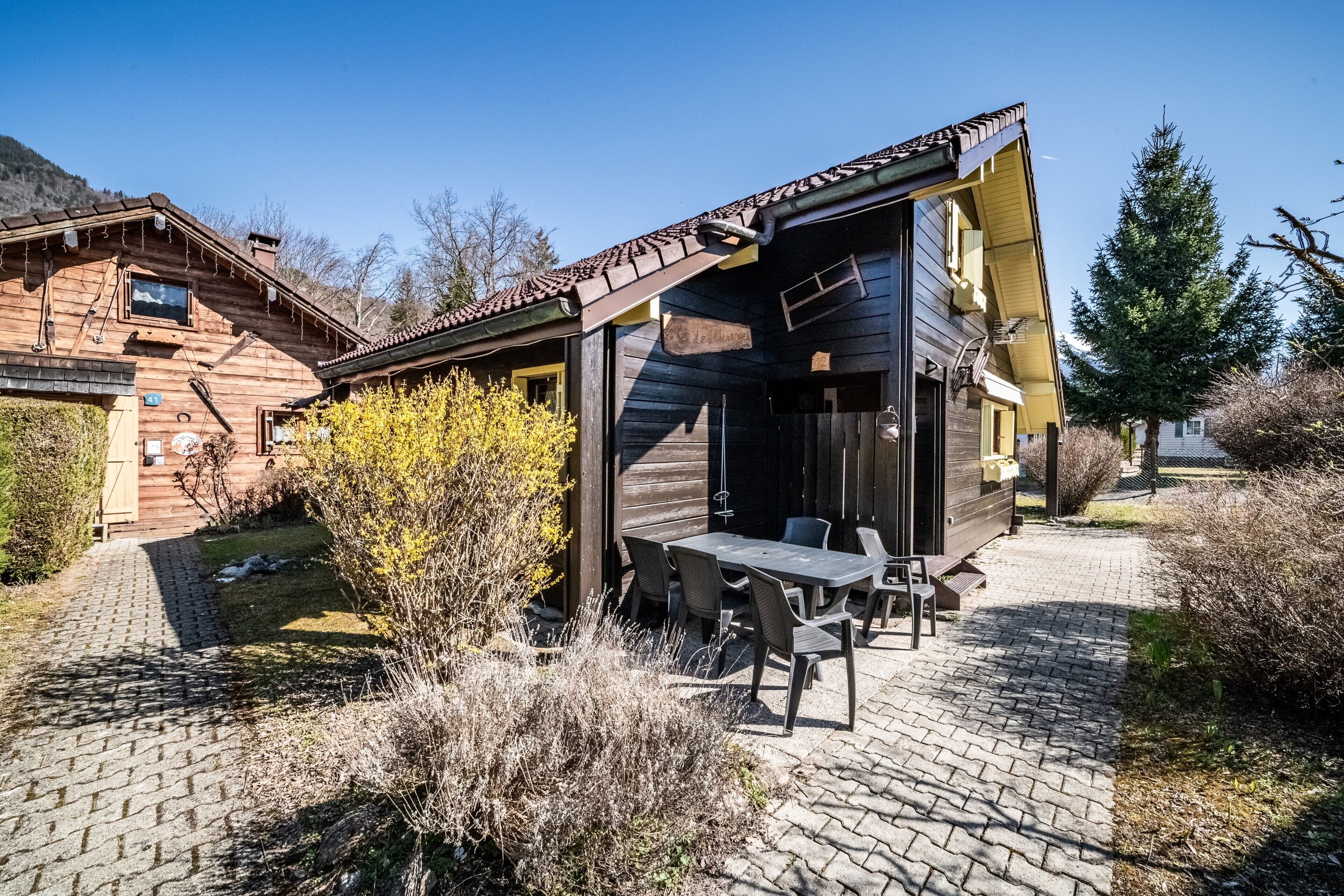 Una cabaña de madera con un patio, mobiliario exterior y montañas al fondo.