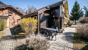 A wooden cabin with a patio, outdoor seating, and a mountain backdrop. - Chalet “8p Simple - Les Mésanges” with Mountain View, Private Terrace, and Wi-Fi (Verchaix)