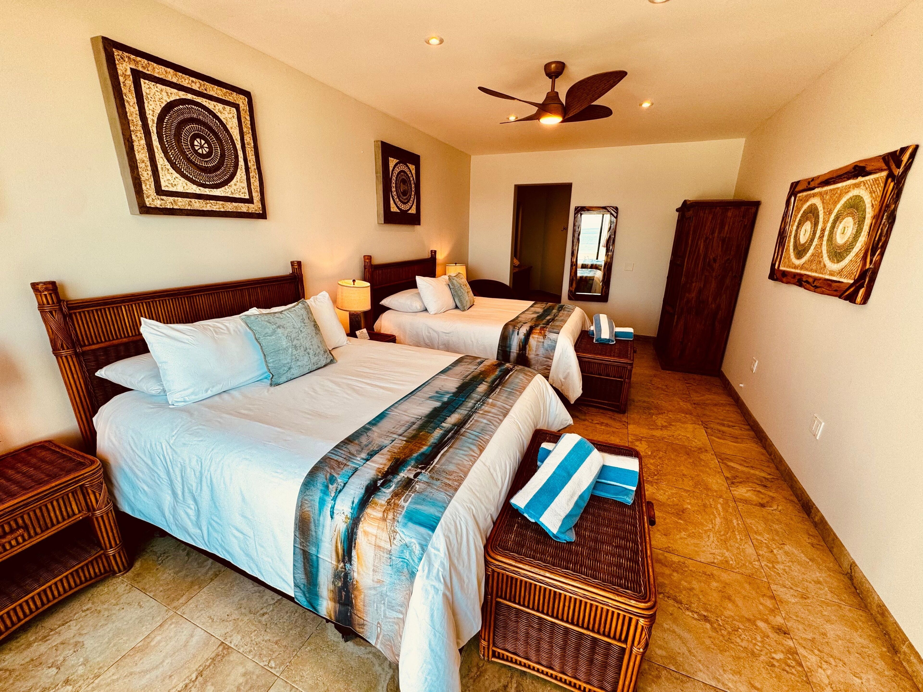 A hotel room with two beds, a ceiling fan, and artwork on the walls.