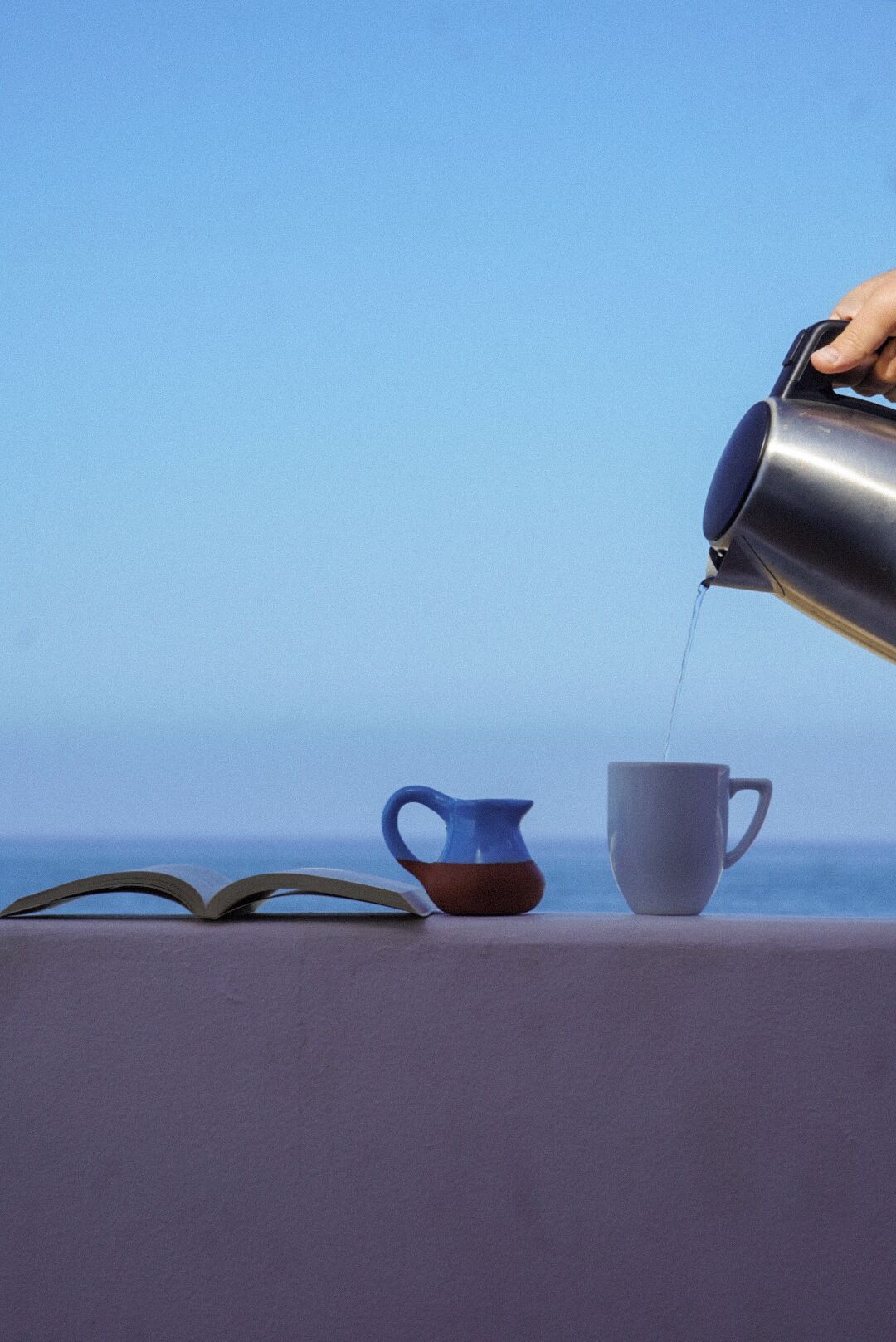 A table with a book, a blue pitcher, and a white cup.