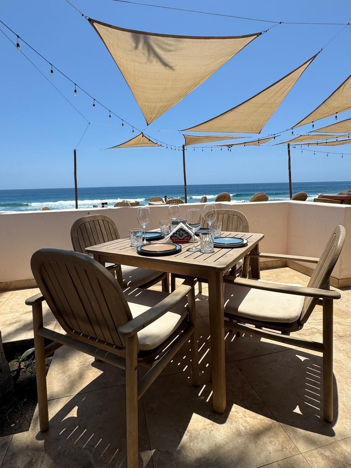Zona pranzo all'aperto con tavolo imbandito per due persone, sedie e vista sull'oceano.