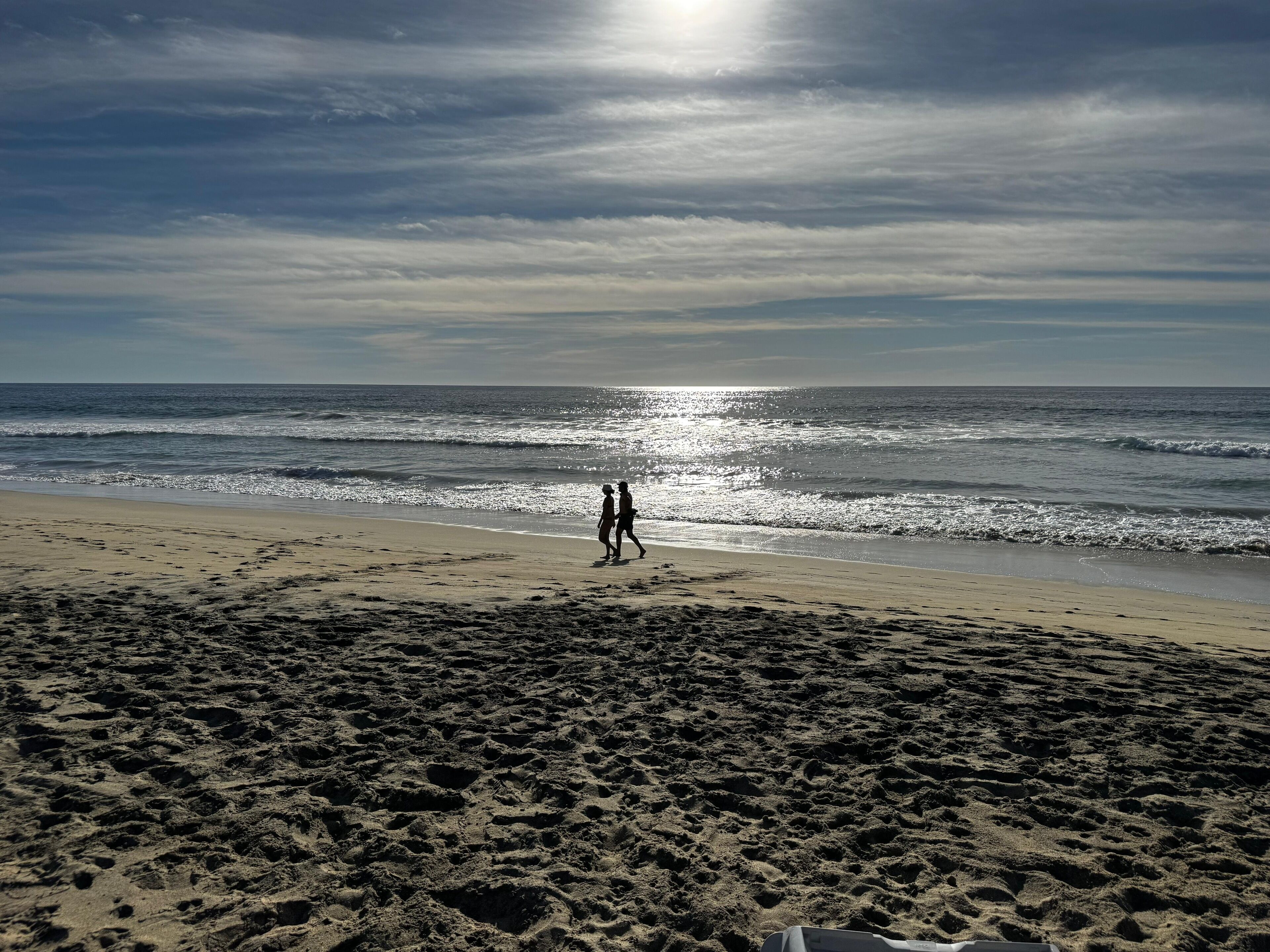 Une plage où l’on voit des empreintes de pas menant à l’eau, un ciel dégagé et le soleil se reflétant sur la mer.