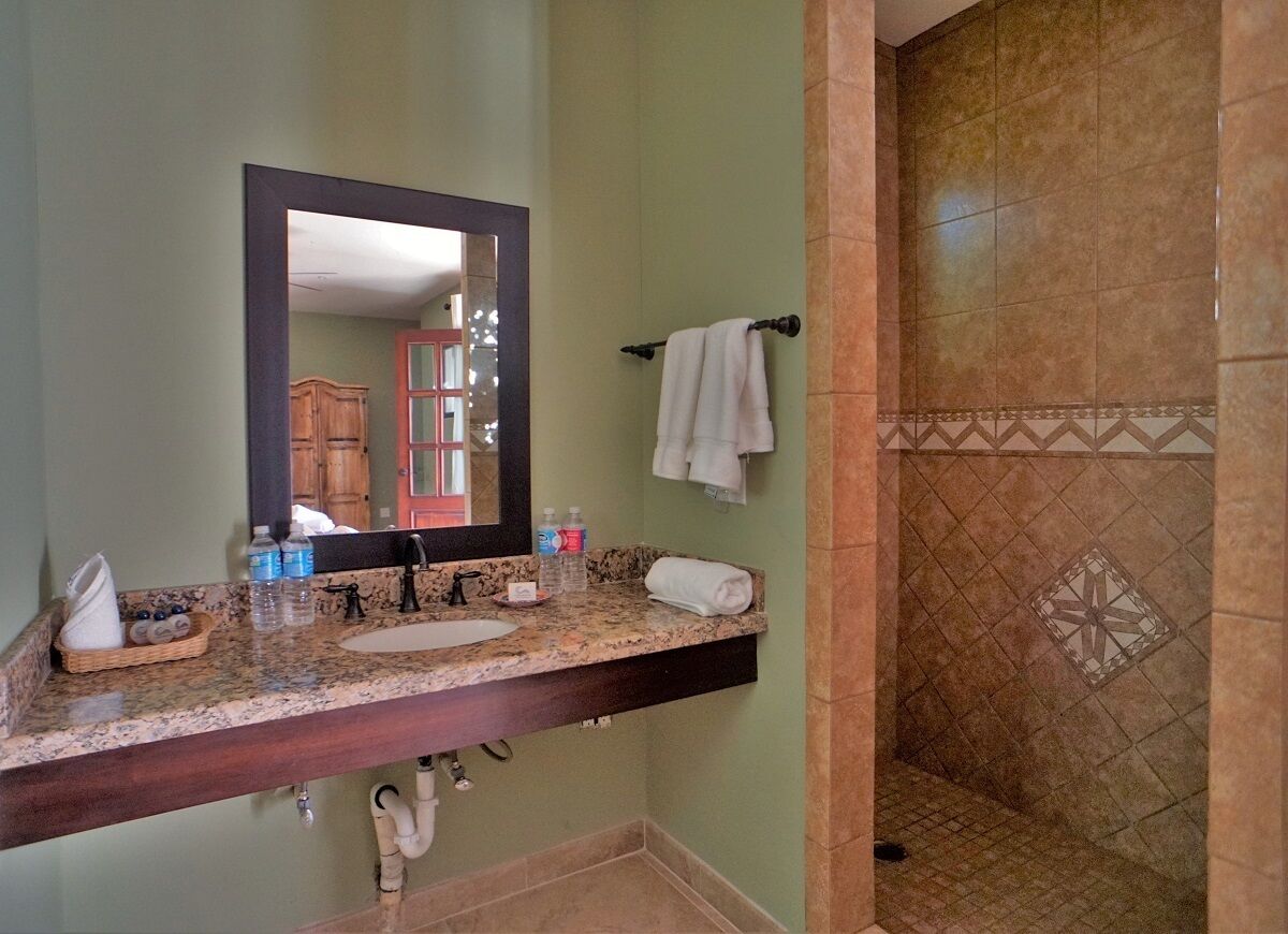 A bathroom with a granite countertop, a sink, a mirror, a towel rack, and a shower with patterned tiles.