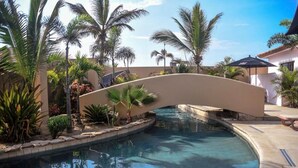 A pool area with a curved bridge, palm trees, and a clear blue pool.