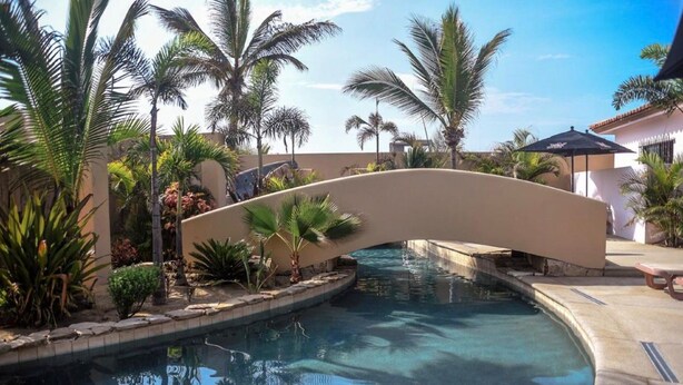 A pool area with a curved bridge, palm trees, and a clear blue pool. - The Cerritos Beach Inn (El Pescadero)