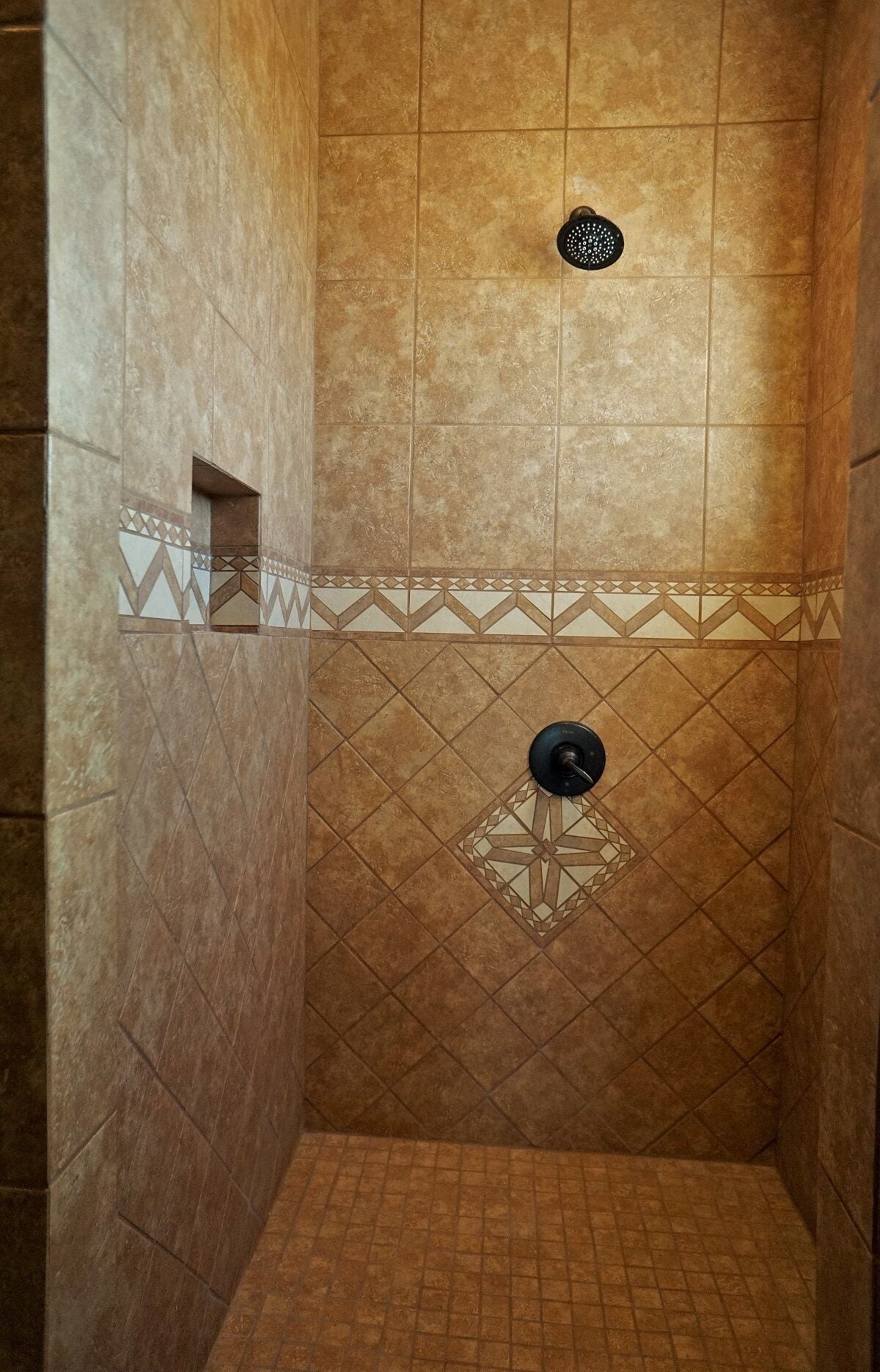 A shower with a geometric tile pattern and a showerhead.