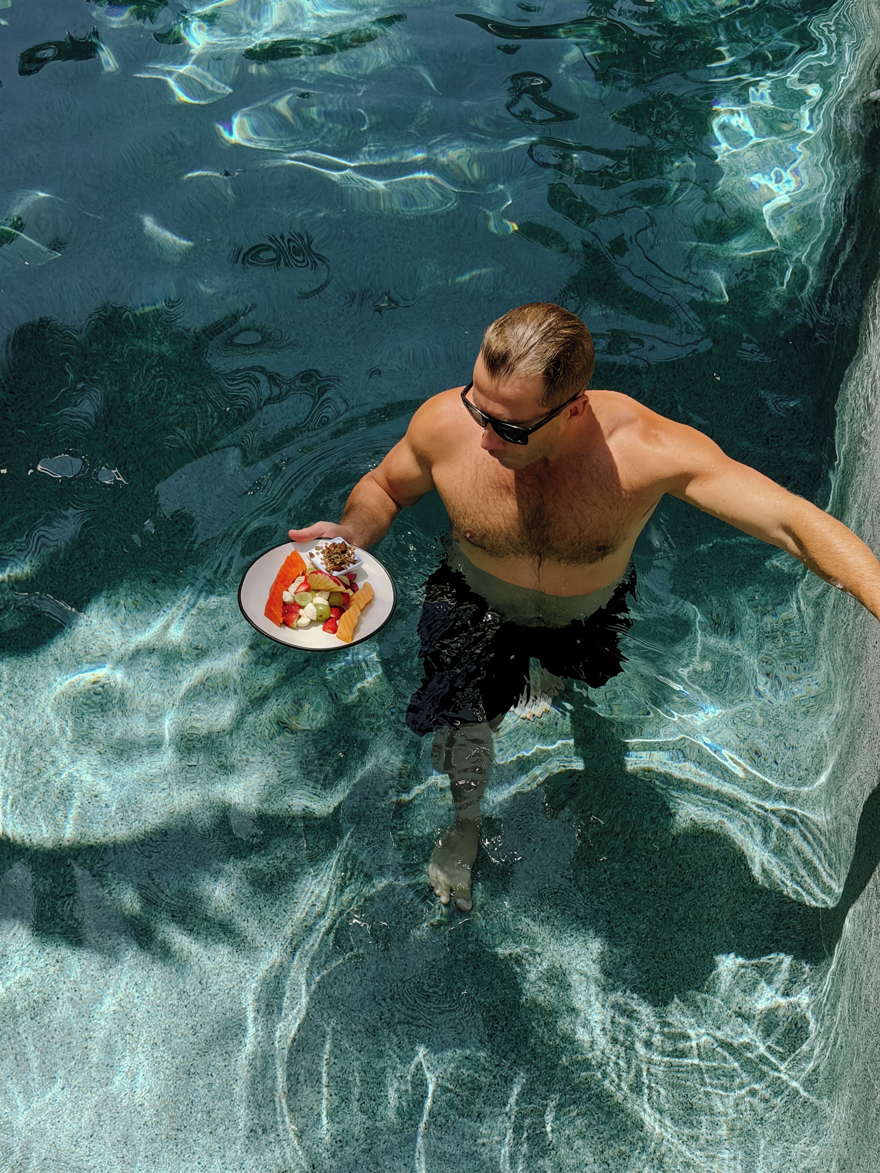 A man in a swimming pool holding a plate with food.