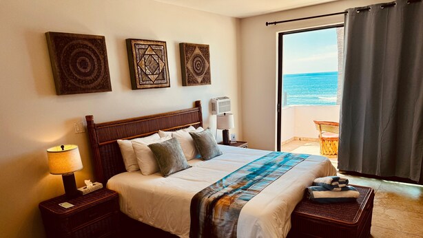 Ein stilvoll eingerichtetes Hotelzimmer mit einem großen Bett, Blick auf den Ozean und drei Wanddekorationen.